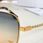 Sunglasses close-up: gold-tone frame with chain temple and engraved logo on the bridge