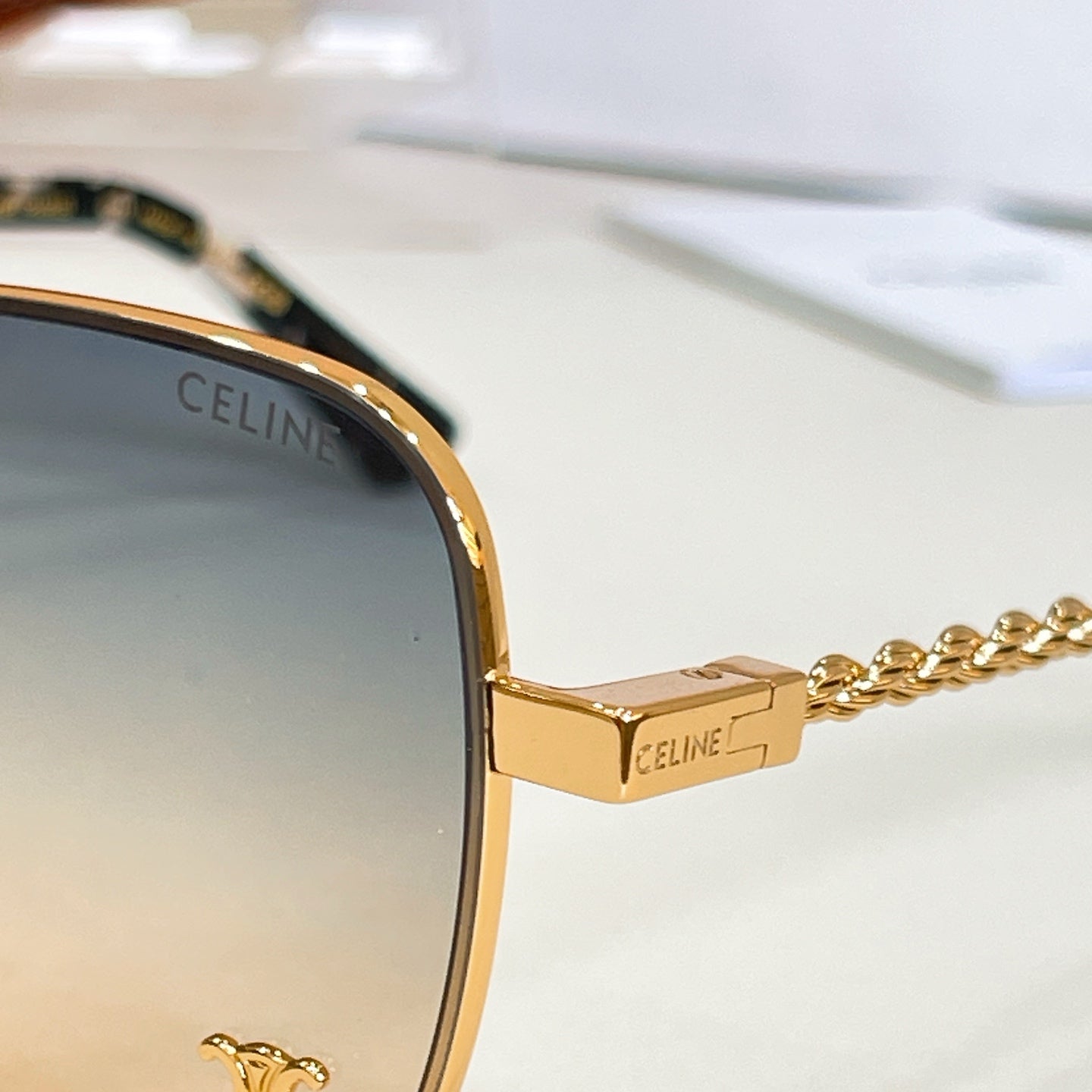 Sunglasses close-up: gold-tone frame with chain temple and engraved logo on the bridge