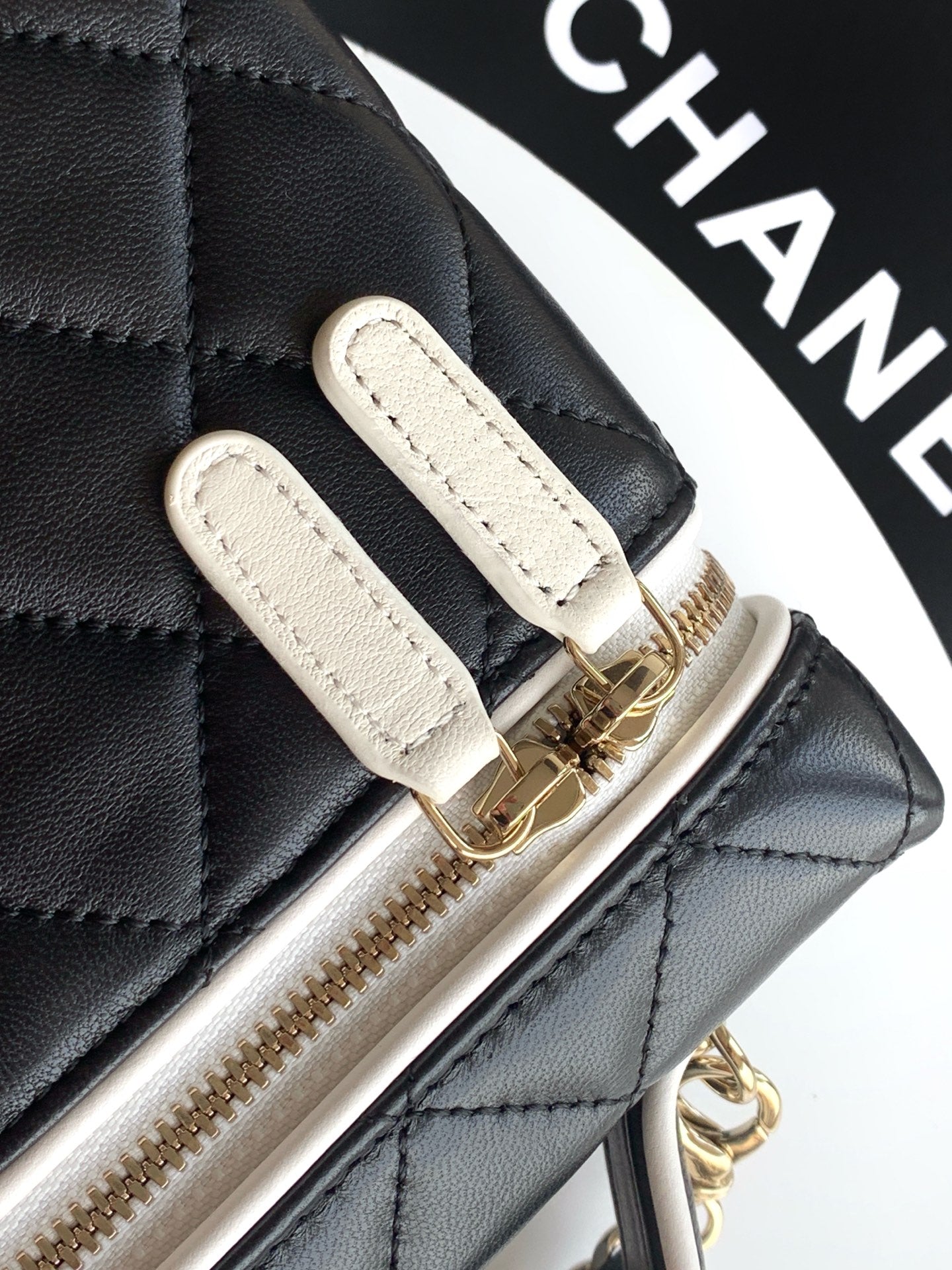 Black quilted bag edge with white leather tabs and gold-tone chain zipper pull