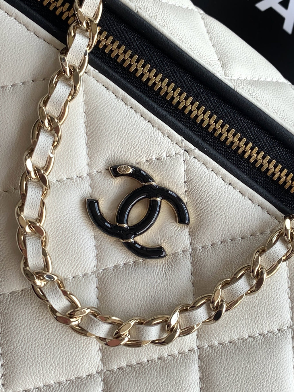 Close-up of quilted bag logo and chain detail with black zipper pull