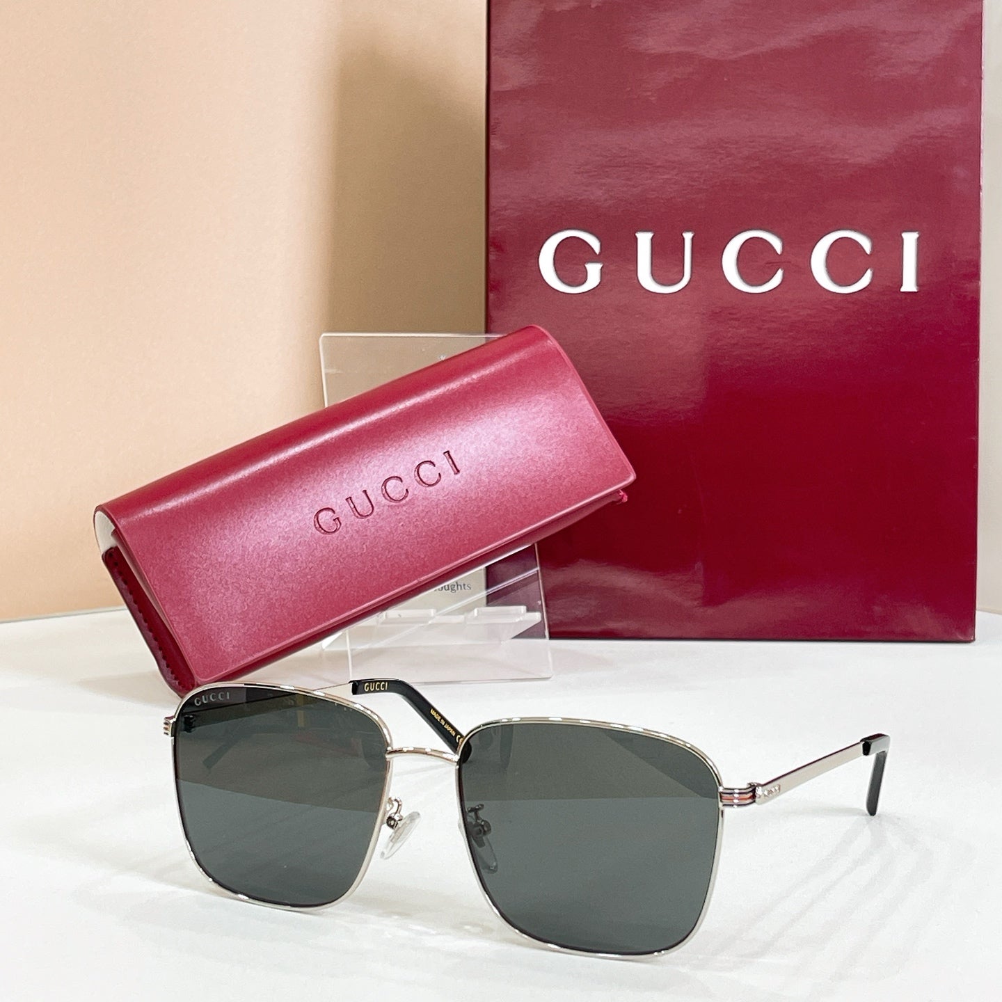 Square sunglasses with silver frame and dark gray lenses, with pink logo case