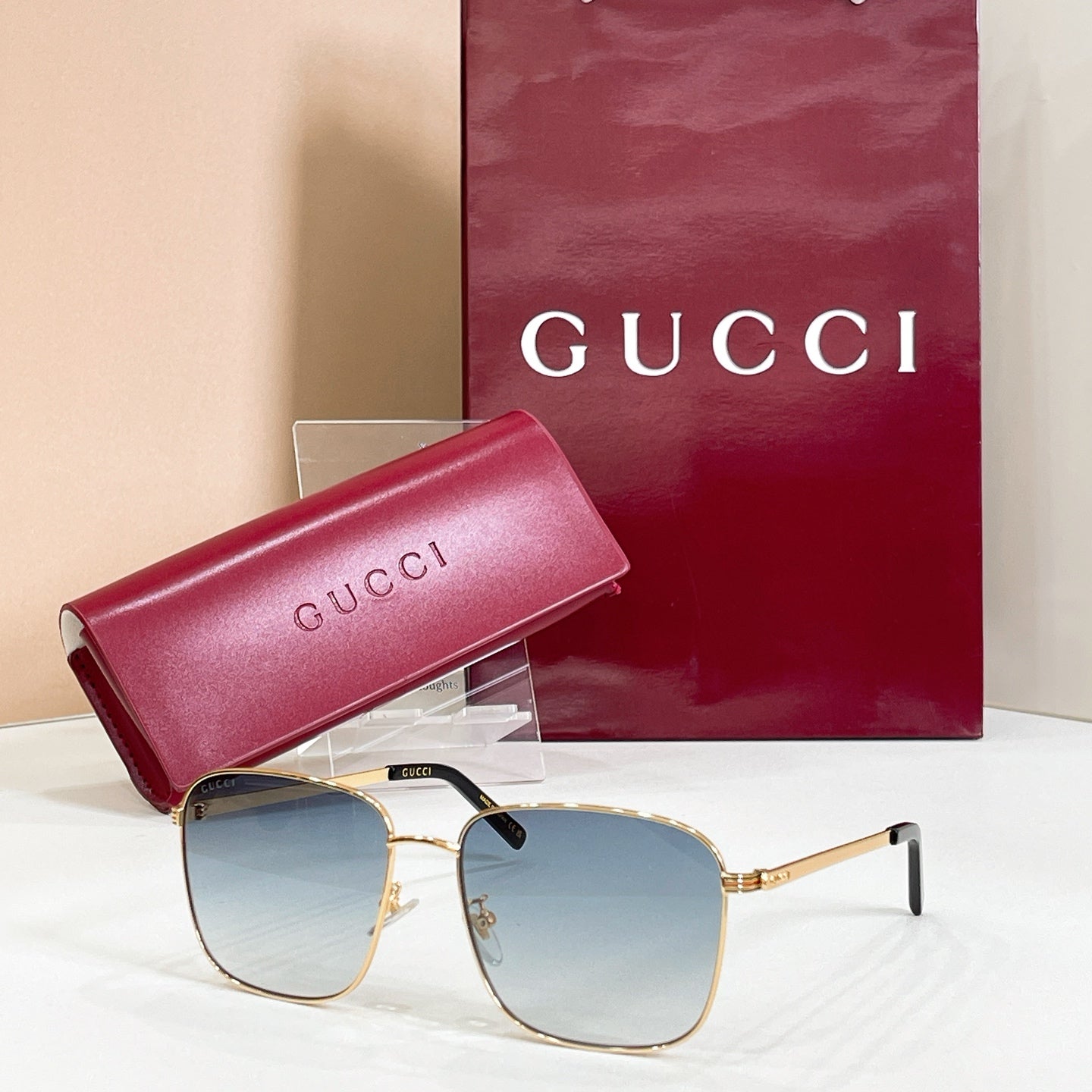 Square sunglasses with gold frame and light blue lenses, with pink logo case