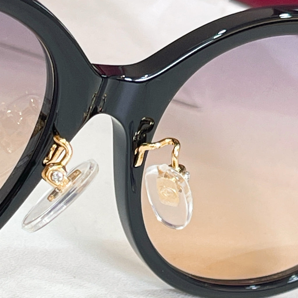 Black sunglasses frame close-up with gold-tone logo details and tinted lens