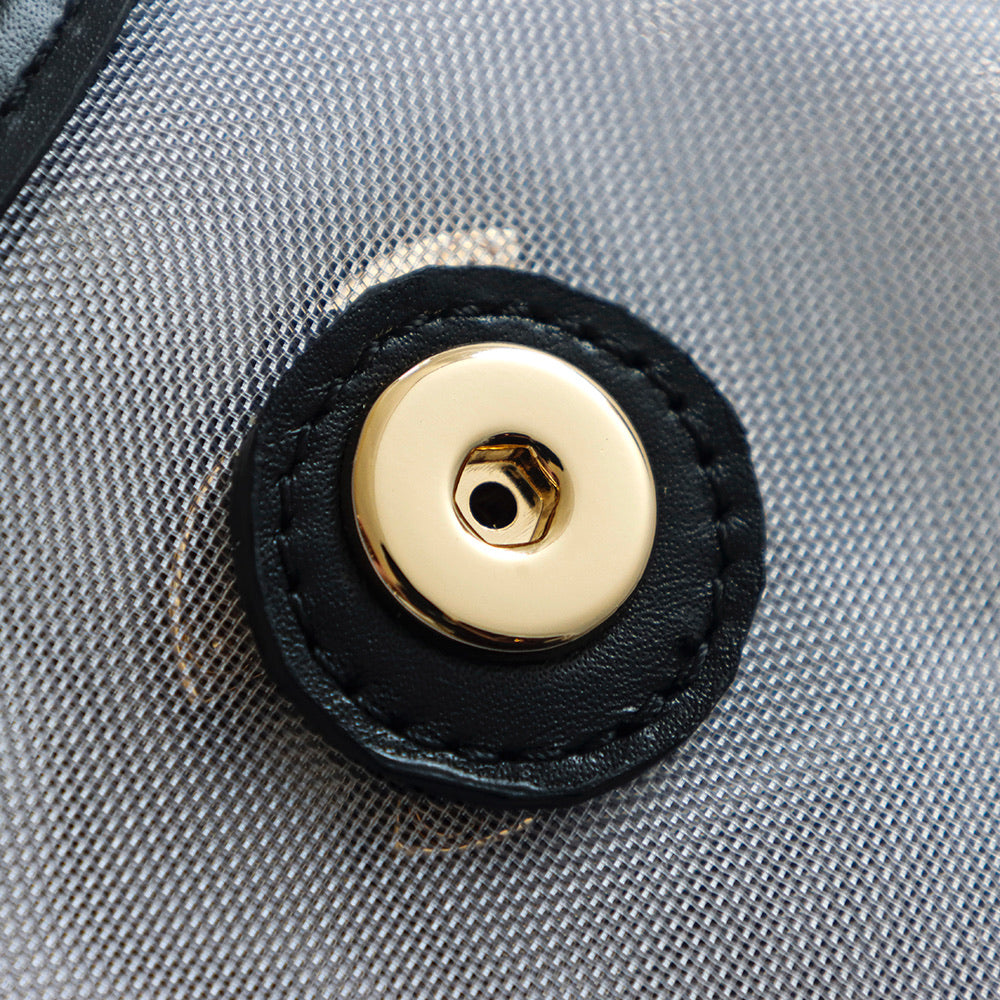 Round gold-tone snap button on light textured fabric with black leather trim