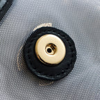 Round gold-tone snap button on light textured fabric with black leather trim