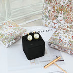 Pair of pearl drop earrings with gold-tone posts, shown on a black presentation box.