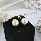 Pearl drop earrings with gold-tone hooks and large round white pearls on a display box.