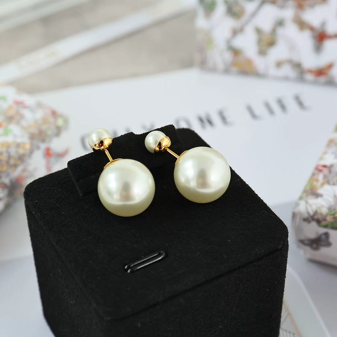 Pearl drop earrings with gold-tone hooks and large round white pearls on a display box.