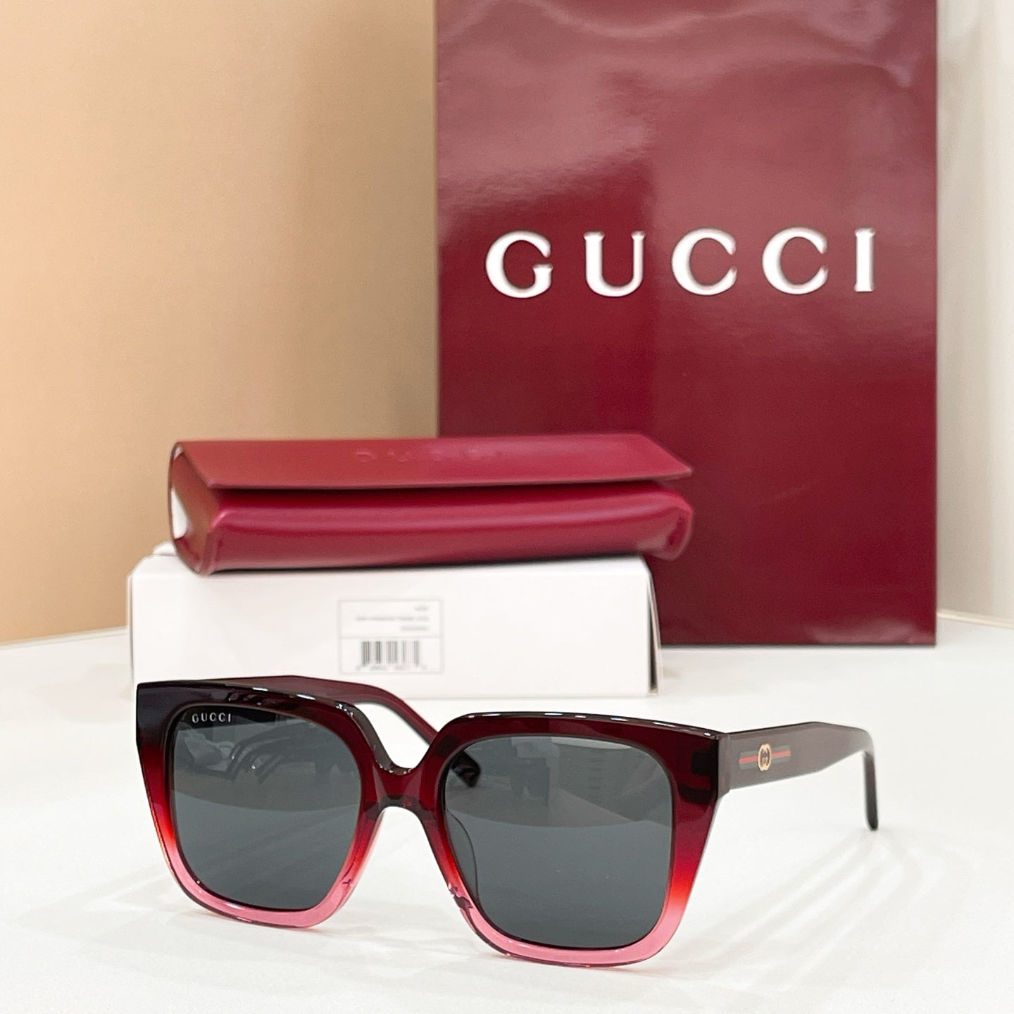 Burgundy square sunglasses with dark tinted lenses, wide frames and gold logo detail