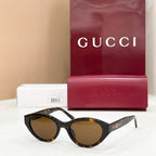Black cat-eye sunglasses with dark lenses, Gucci logo on temples and gold accents.