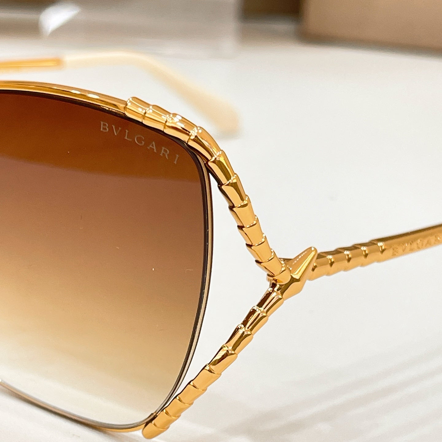 Gold-tone sunglasses close-up with engraved BVLGARI on the temple and tinted lenses