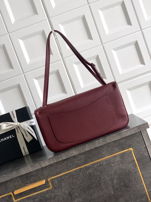 Burgundy Chanel shoulder bag with long strap and flap front with gold-tone CC clasp.