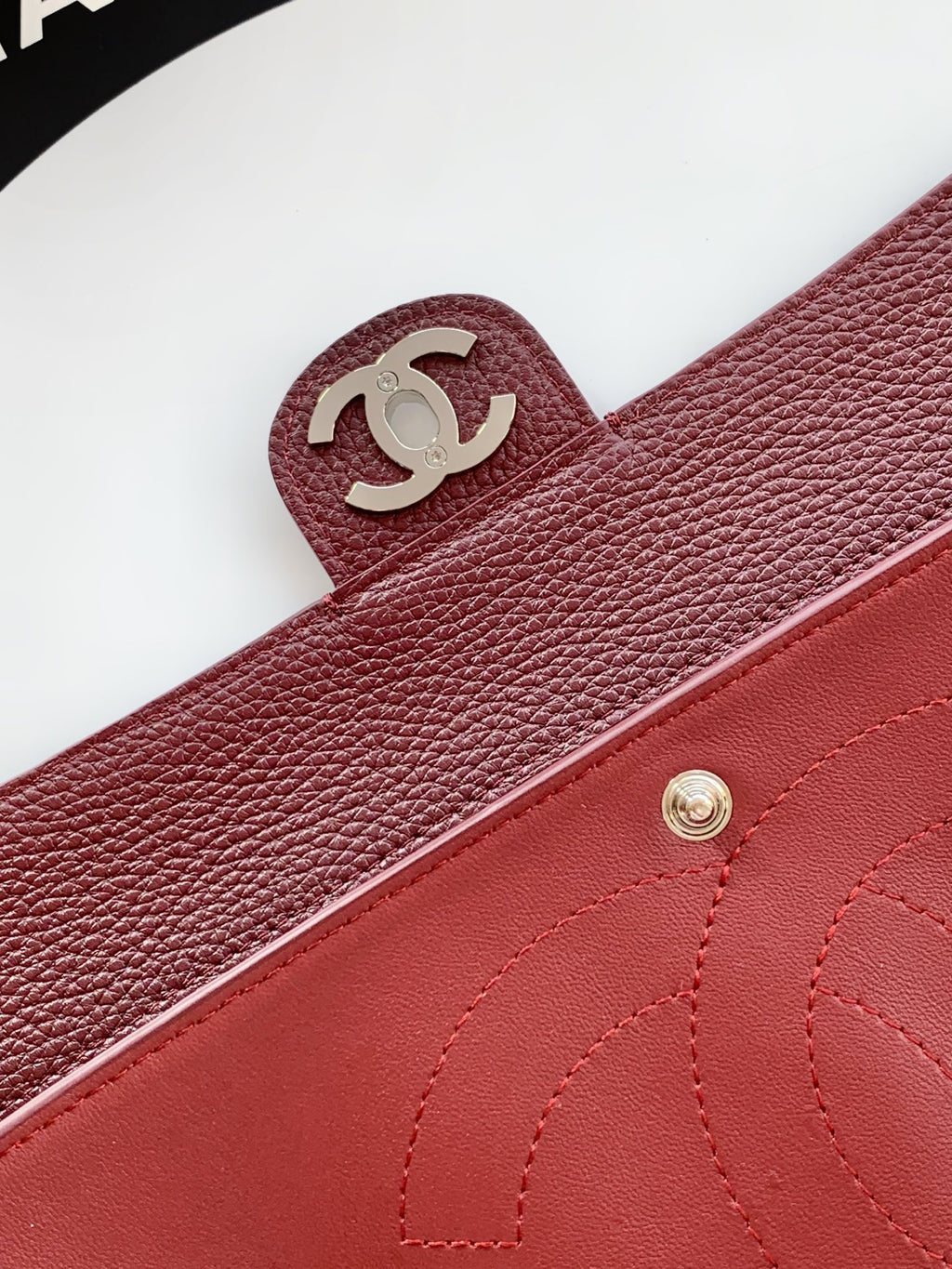 Burgundy Chanel bag with CC logo strap tab and stitched leather trim.