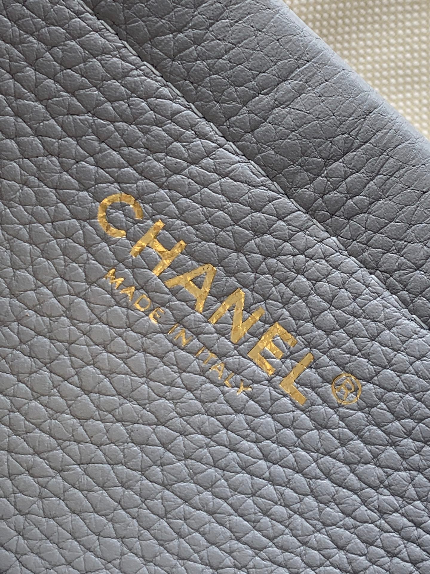 Chanel logo embossing on light gray quilted leather with gold lettering