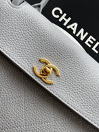 Chanel leather bag closeup: gold CC turn-lock on light gray textured leather
