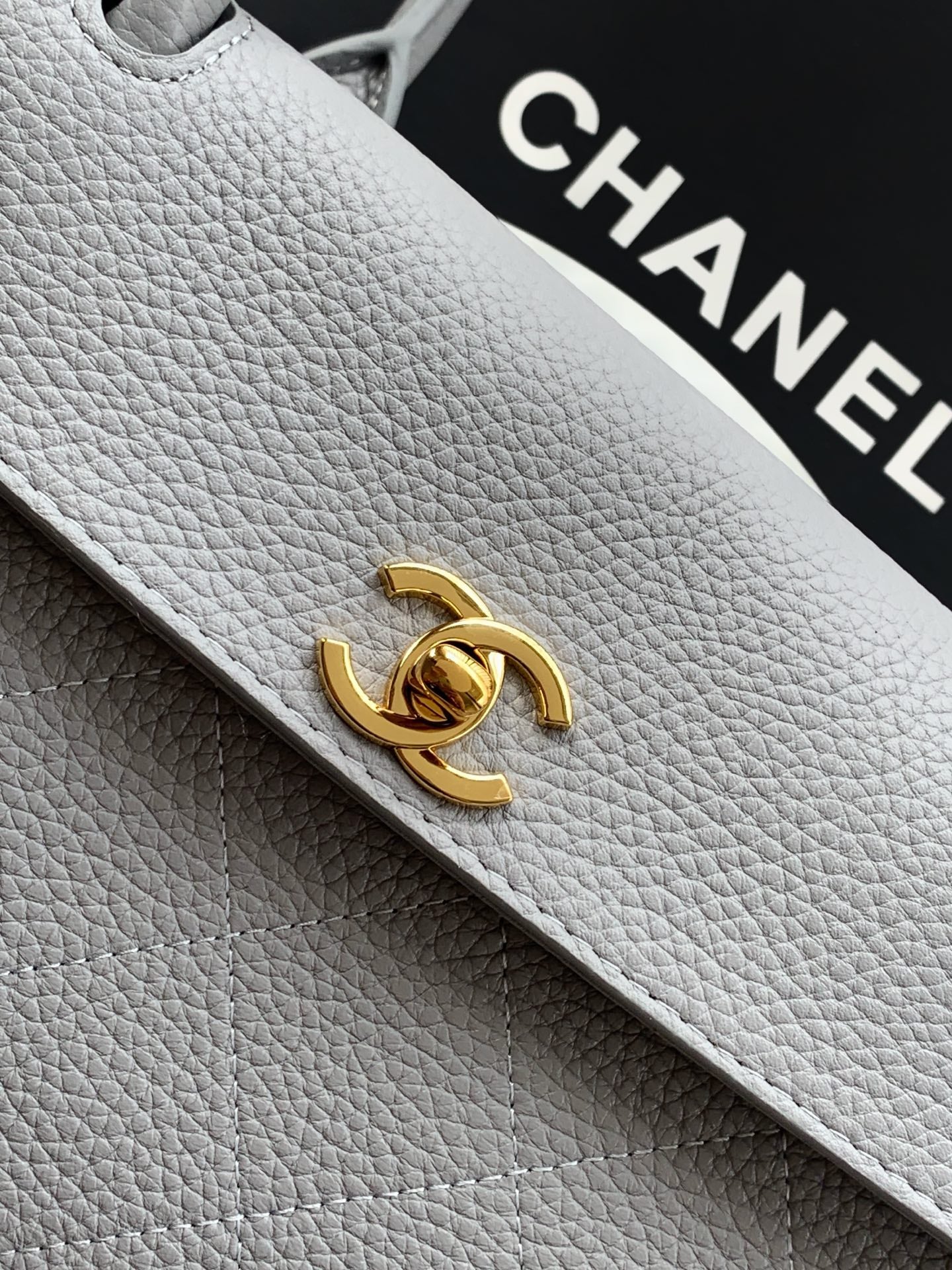 Chanel leather bag closeup: gold CC turn-lock on light gray textured leather