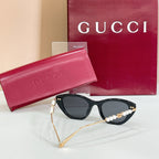 Sunglasses with black lenses, glossy dark frames, and pearl gold temple trim