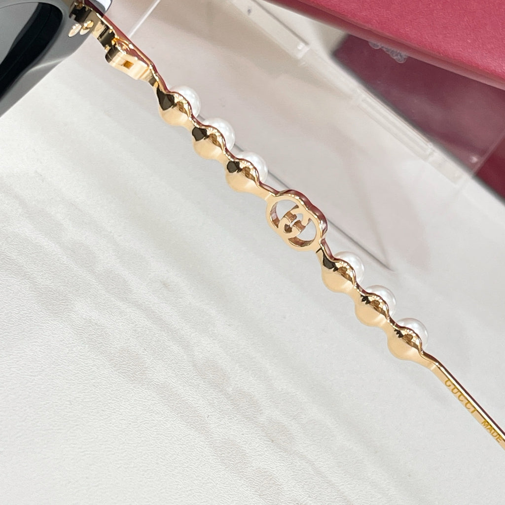 Sunglasses arm close-up with gold logo medallion and chain link detailing