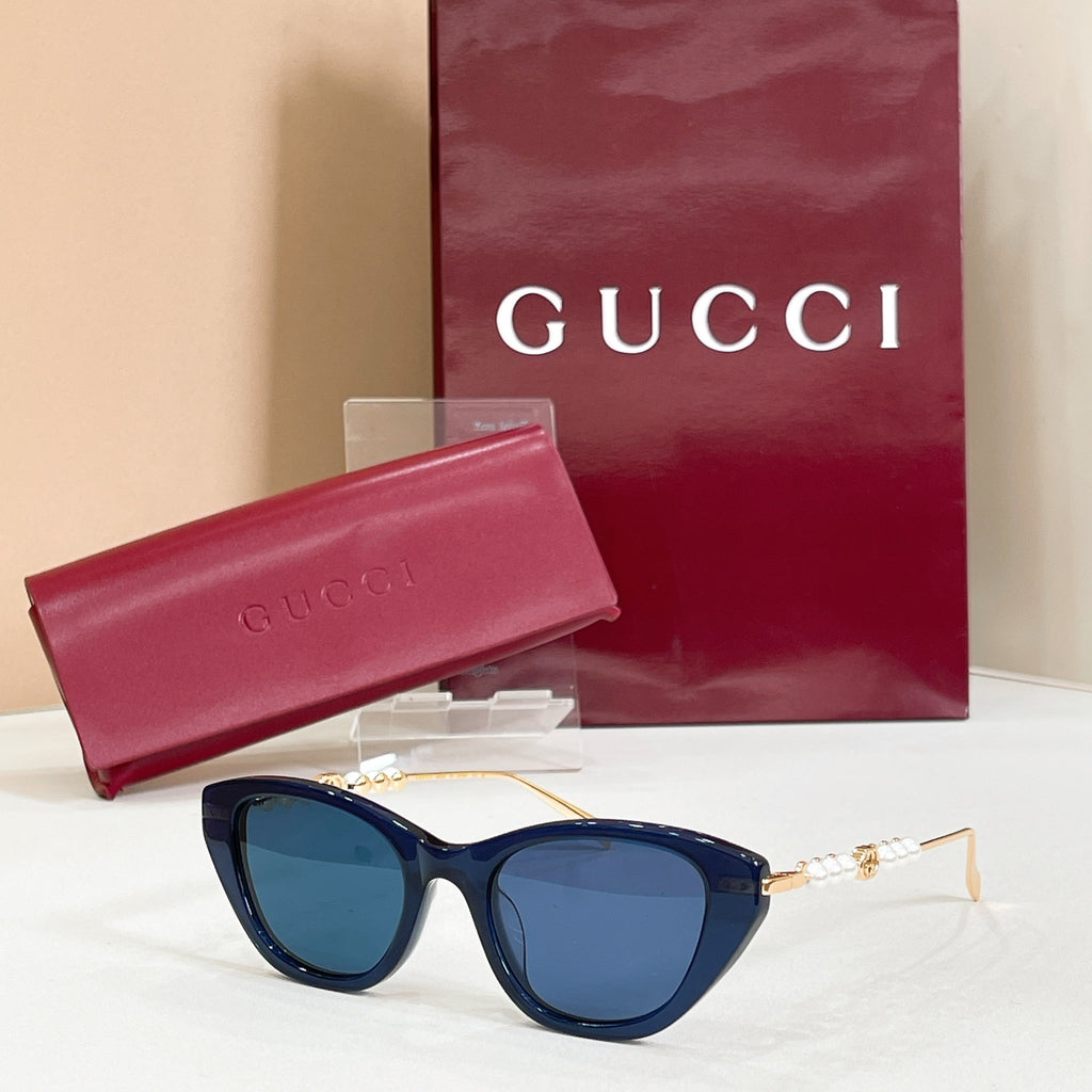 Gucci sunglasses with dark blue lenses, gold frames, and pearl detail on temples