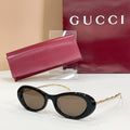 Gucci sunglasses with dark lenses and black oval frames, with gold chain-style temples
