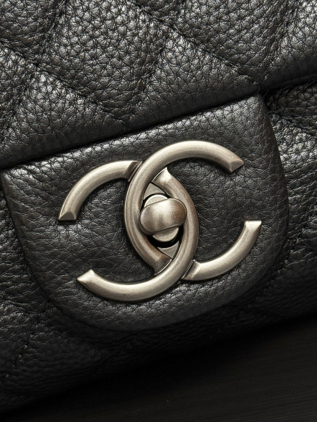 Chanel CC metal logo on dark quilted leather flap.