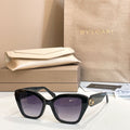 Black square glasses with dark lenses and gold-tone accent on the temple.