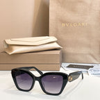 Black square glasses with dark lenses and gold-tone accent on the temple.