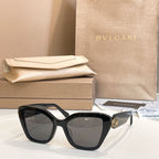 Black square glasses with tinted lenses and gold-tone emblem on the temple.