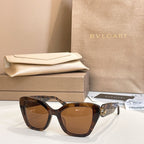 Dark tortoiseshell square glasses with amber-tinted lenses and gold-tone temple emblem.