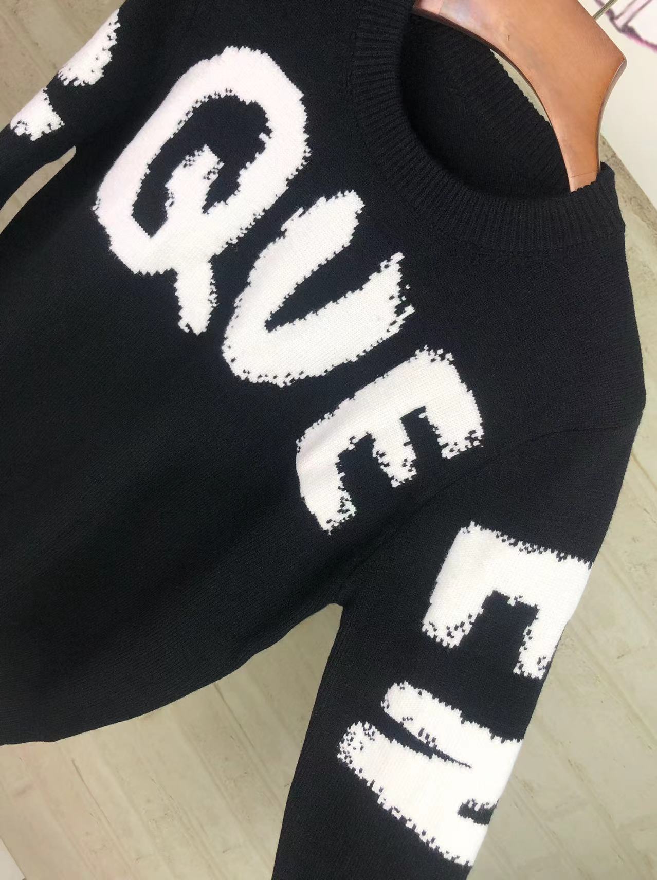 Alexander McQueen knit sweater closeup with white QVE lettering on black