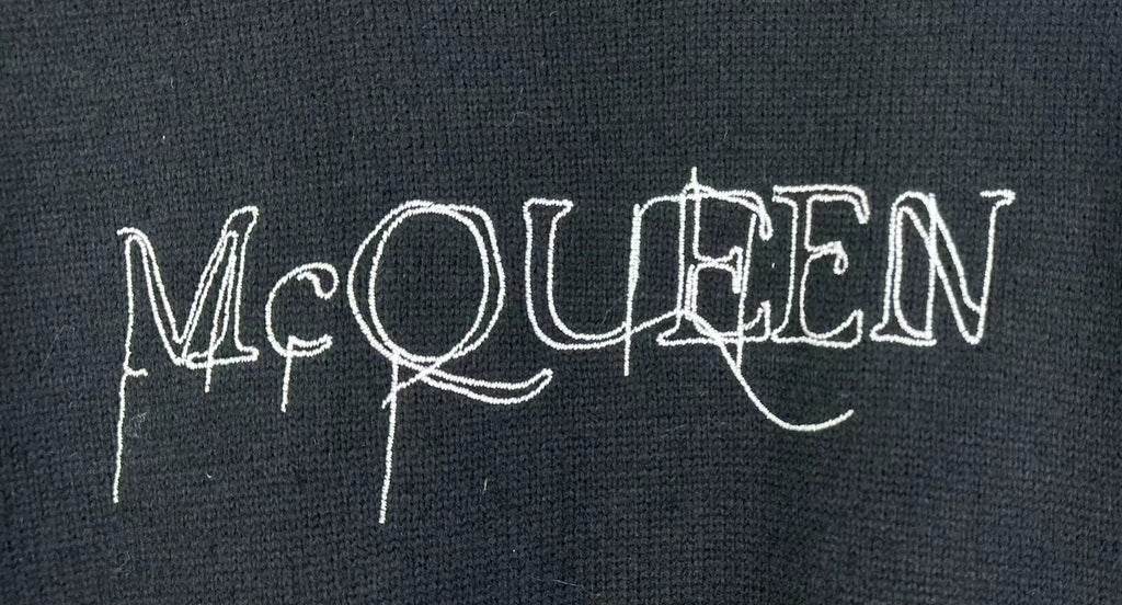 Dark knit sweater close-up with McQUEEN logo graphic across front