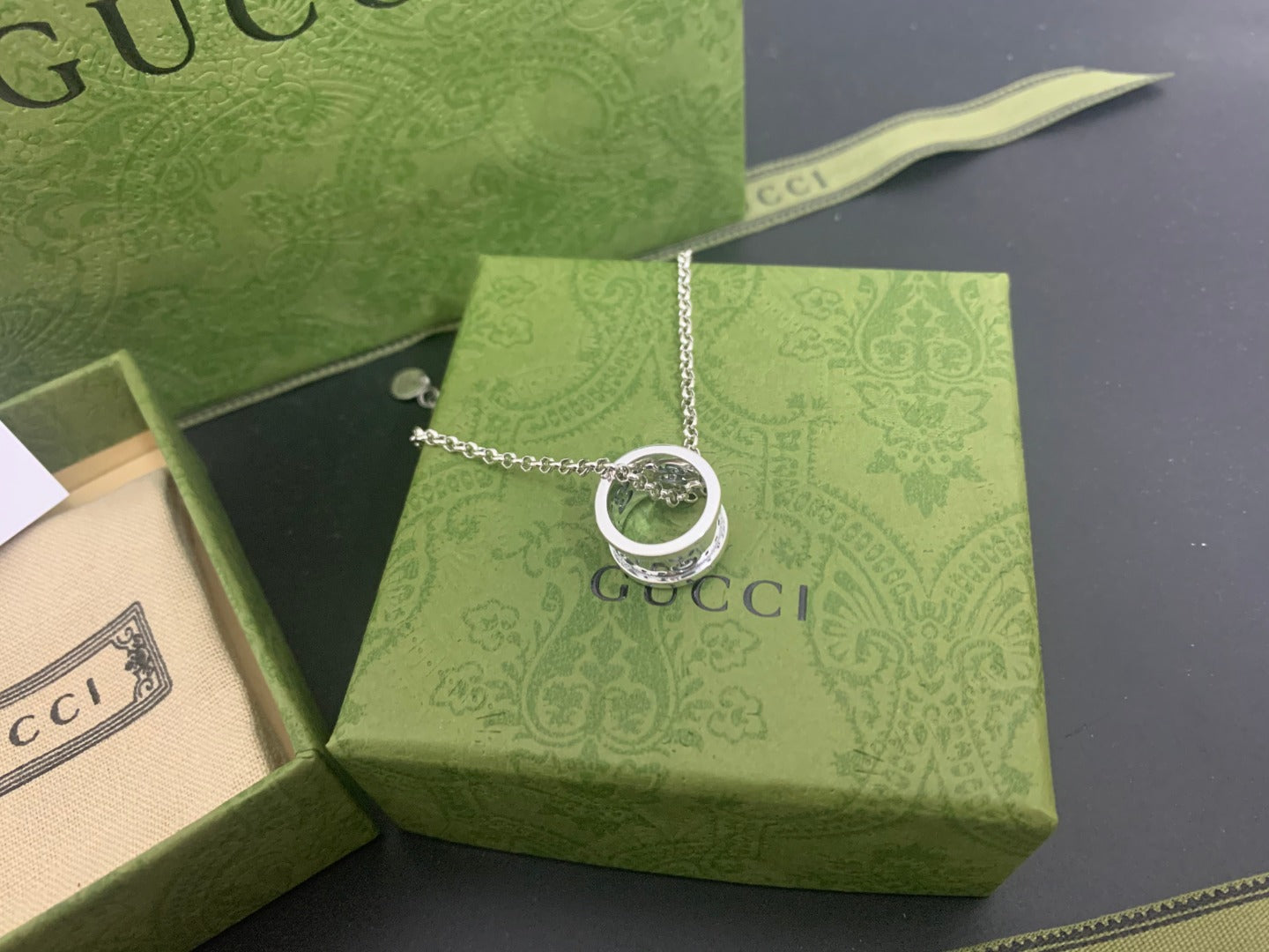 Silver Gucci pendant necklace with circular ring charm on green box