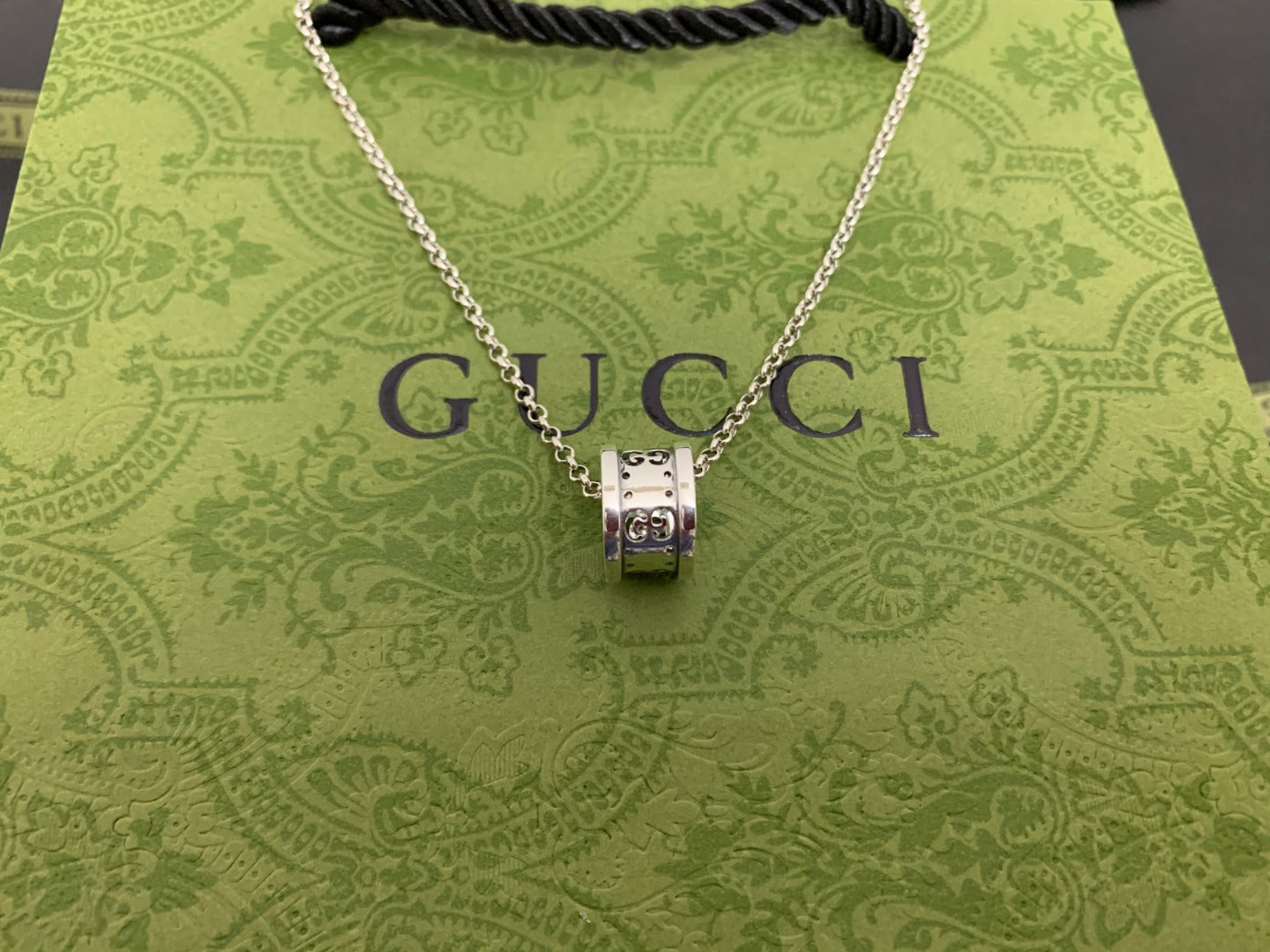 Silver Gucci pendant necklace on green Gucci pouch with large logo