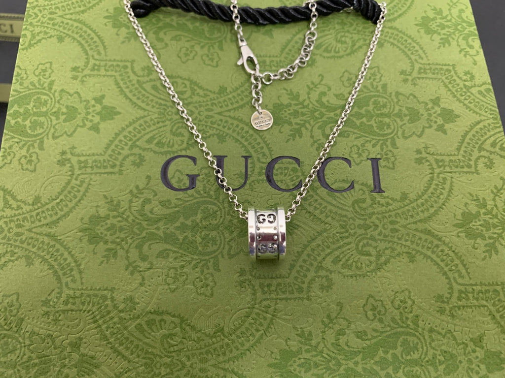 Silver Gucci pendant necklace with chain and black cord on green Gucci pouch