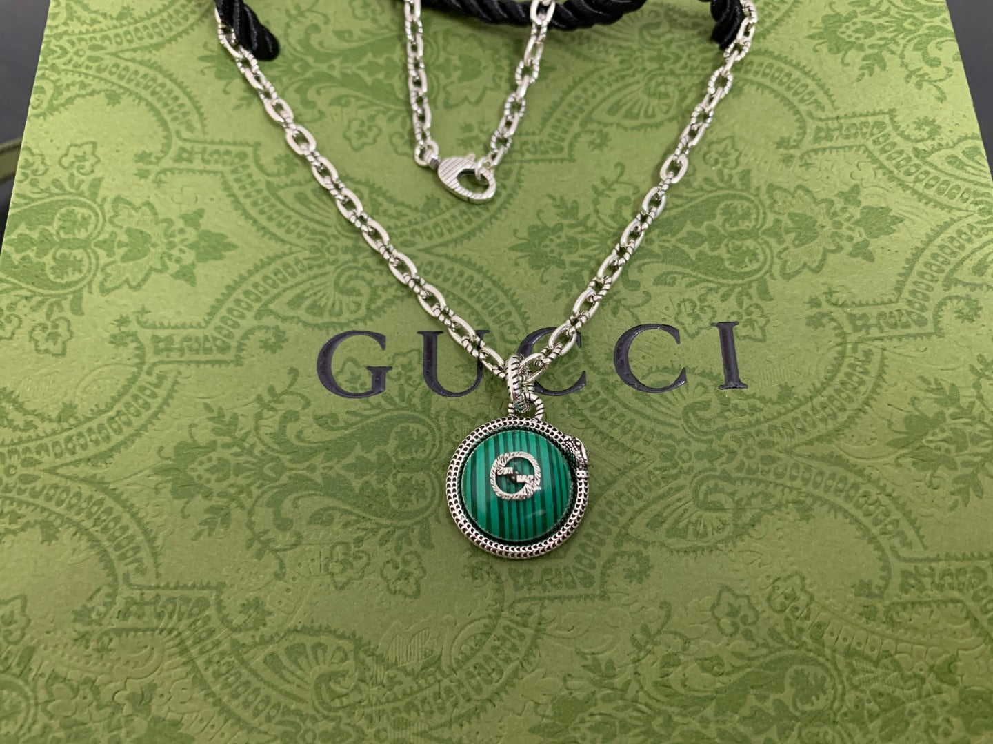 Gucci pendant necklace close-up with green medallion pendant on silver chain