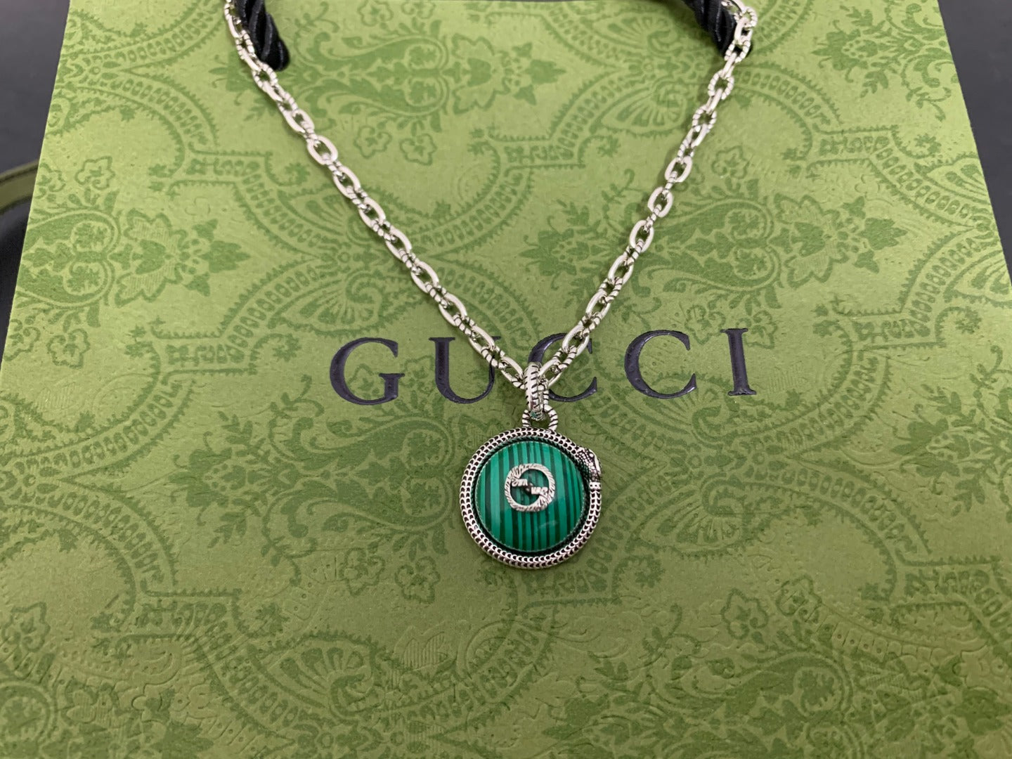 Gucci pendant necklace close-up with green round medallion and silver chain
