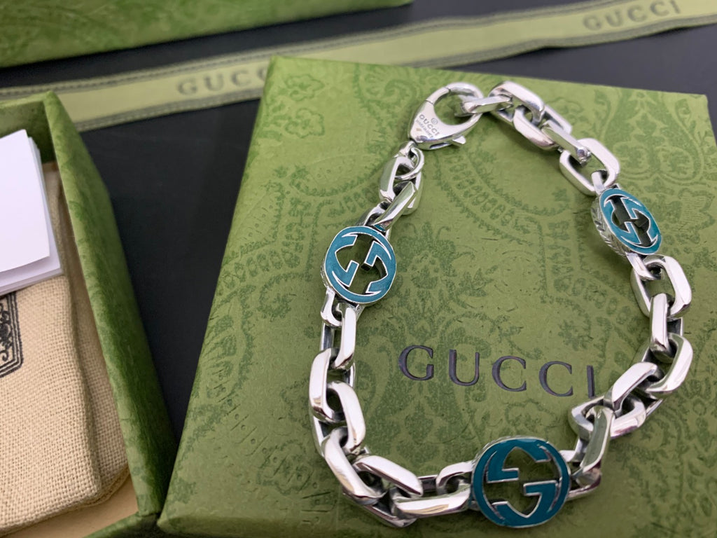 Silver-tone chain bracelet with blue enamel logo medallion links and polished curb links
