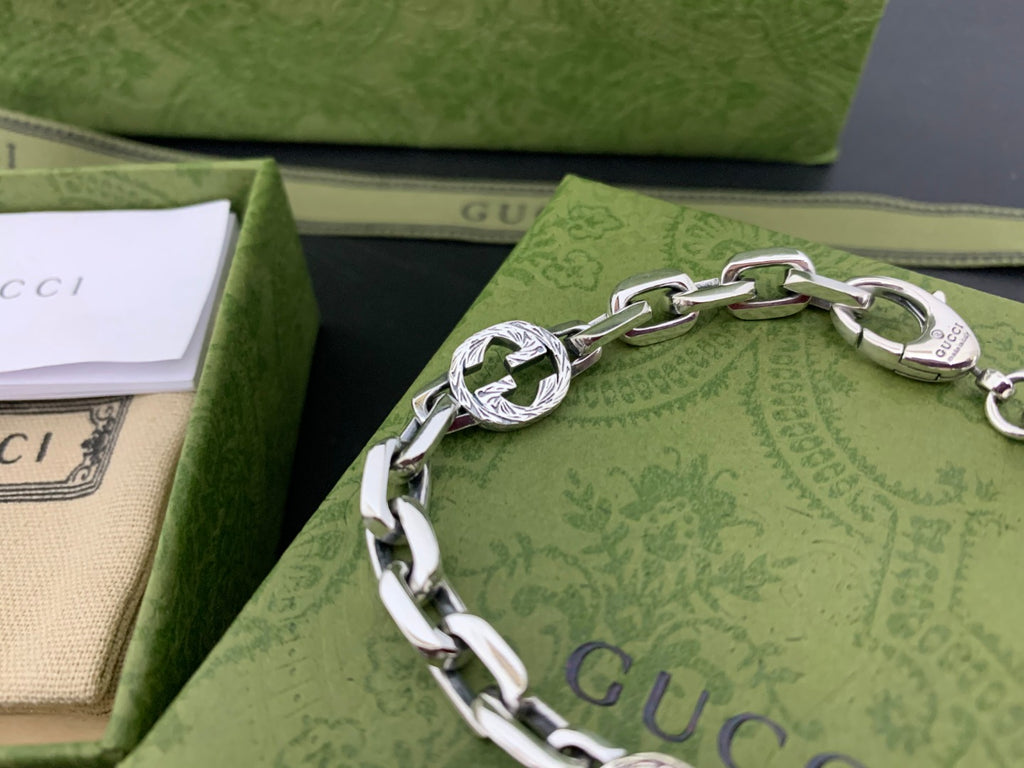 Silver-tone chain bracelet with blue logo medallion links and engraved round clasp, close-up