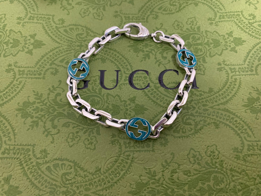 Silver-tone chain bracelet with blue enamel logo discs and oval clasp, centered