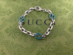 Silver-tone chain bracelet with blue enamel logo discs and oval clasp, centered