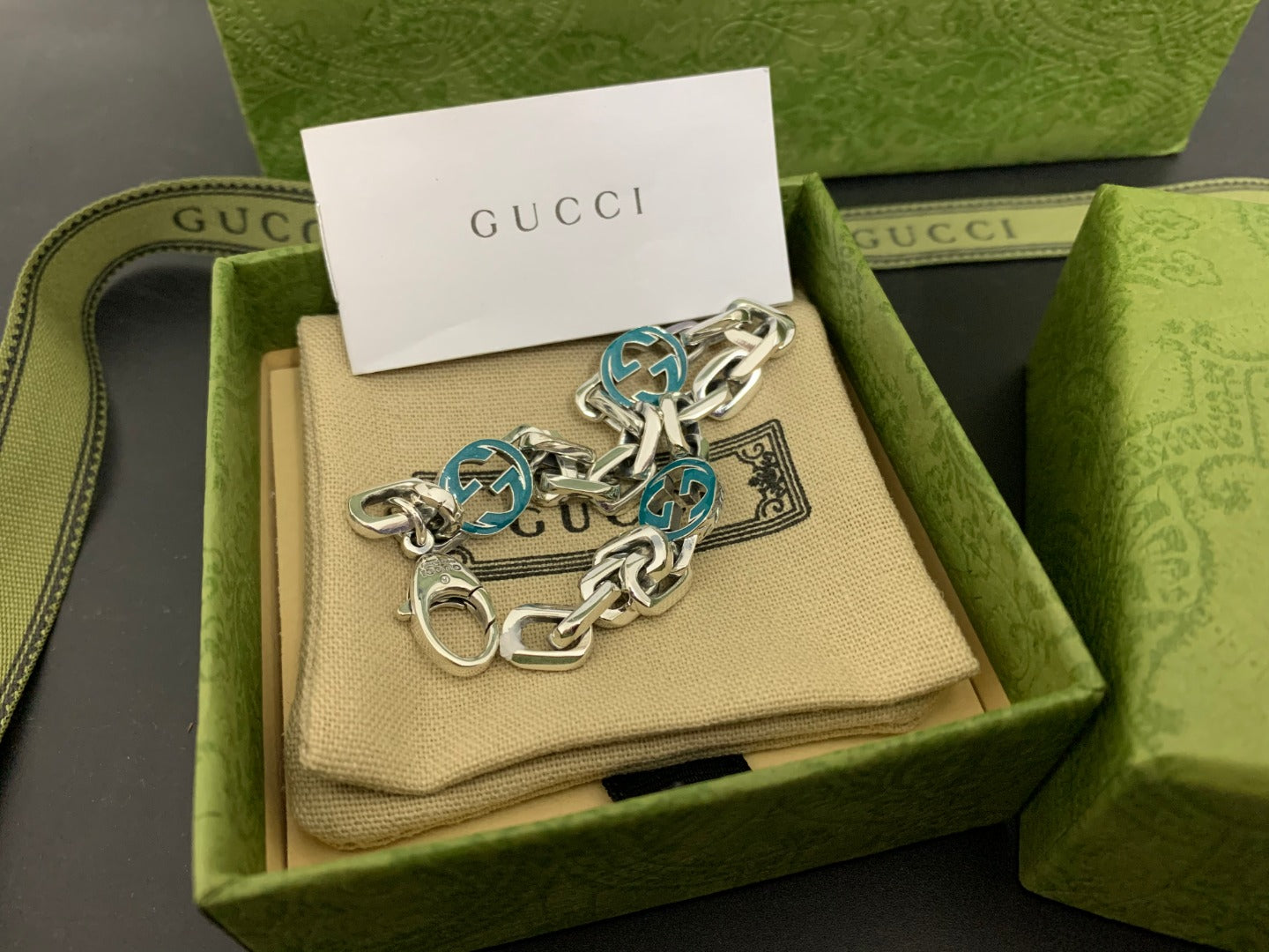 Silver-tone chain bracelet with blue enamel logo discs and round clasp, angled view