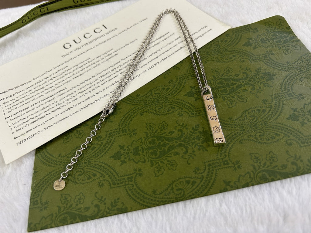 Gucci necklace with silver chain, rectangular GG pendant, and small round charm