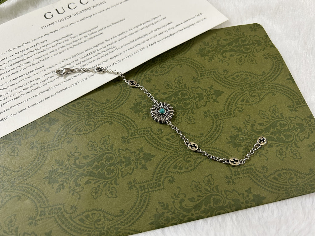 Silver link bracelet with turquoise flower charm and small round logo tags.