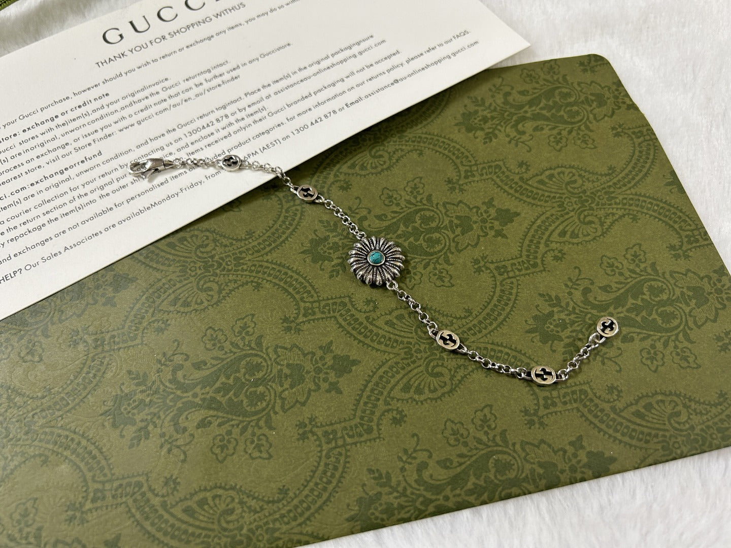 Silver link bracelet with turquoise flower charm and small round logo tags.