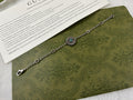 Silver link bracelet with turquoise flower charm and small round logo medallions.