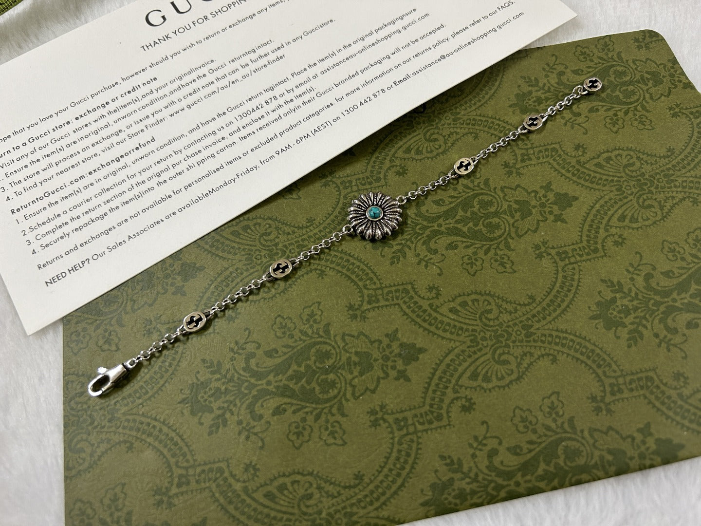 Silver link bracelet with turquoise flower charm and small round logo medallions.