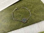 Silver charm bracelet with turquoise flower centerpiece and linked oval logo beads.
