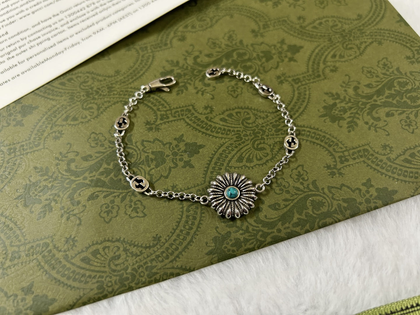 Silver charm bracelet with turquoise flower centerpiece and linked oval logo beads.