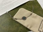Silver charm bracelet with turquoise flower center on beige fabric pouch.