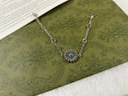 Silver chain bracelet with turquoise flower pendant and oval logo links.